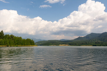 Summer sunny day with fluffy white clouds over lake and mountains 