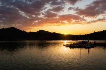 Colorful sunrise over pontoon boat and a cloudy sky, calm lake and mountains. Colibita lake, Romania