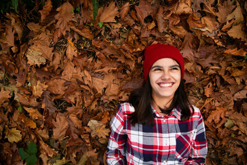 Laughing teen girl lying in a bed of dry leaves in autumn