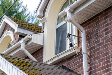 Closeup view of old white gutter system with soffit vent, window with white frame, gutter guard, downspout, decorative trim molding, on corner of brick luxury house © sommersby