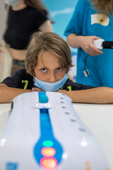 happy focused boy in medical mask trains thought power to win with robotics, vertical