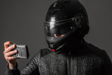 A motorbiker with a mobile phone in his hands on the gray background.