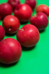 Close up of some fresh red plums on a colorful green surface 