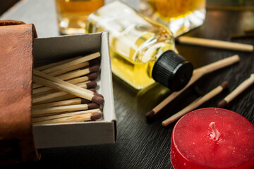 Some wooden matches in a matches box, candles and some glass flovering bottles on a black wooden table 