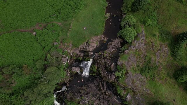 Aerial footage of the Loup of Fintry waterfall, near the village of Fintry in Central Scotland. People wild-water swimming in the pools at the bottom of the cascade.