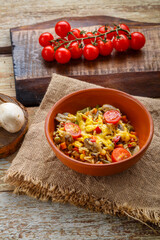 Risotto with mushrooms in a plate on a wooden background on a linen napkin next to tomatoes on a plank.