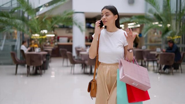 Beautiful happy brunette woman calling her best friend and telling about stylish clothes she bought in fashion boutique, inviting her to go together on shopping during seasonal sales in mall