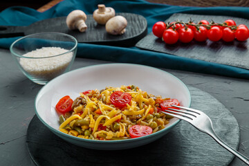 Risotto with mushrooms in a plate on a gray background near the ingredients on black coasters and a fork.