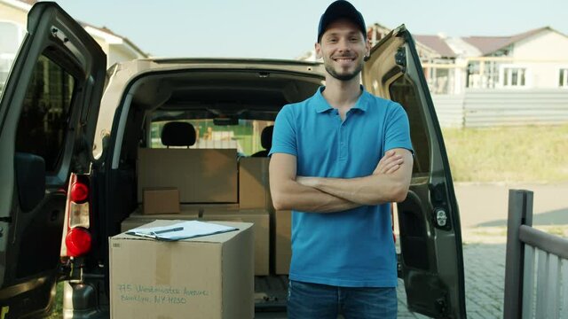 Portrait of delivery guy standing near commercial van full of boxes with arms crossed smiling looking at camera. People and courier service concept.