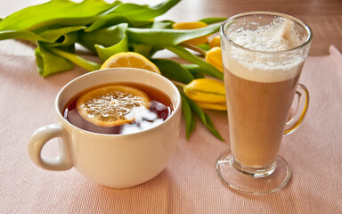 tea and coffee close up with lemonn and yellow tulips in the background