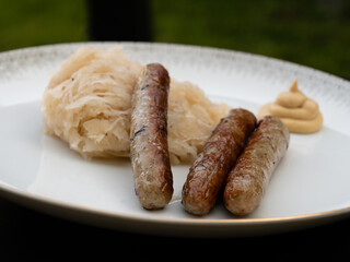 Nuremberg Grilled Sausage or Nürnberger Rostbratwurst with Sauerkraut or Sour Cabbage and Mustard on a White Plate Side View