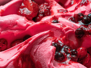 Frozen Forest Fruits flavour gelato - full frame detail. Close up of a pink surface texture of Ice cream covered with pieces of red fruit.