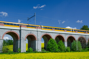 Beautiful scene of viaduct type of bridge with yellow train surrounded by green fields