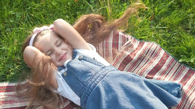 Pretty little child girl with closed eyes laying down on blanket on green grass in summer taking a nap.