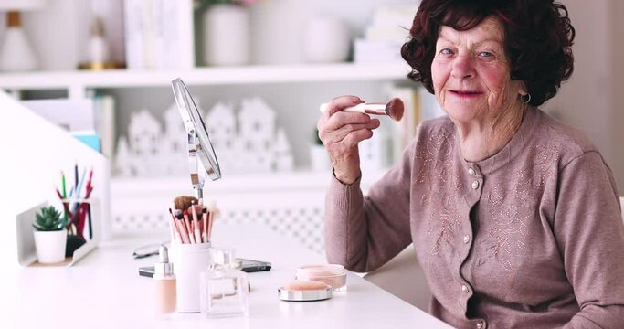 cheerful senior woman applying her makeup on, sitting at the desk at home