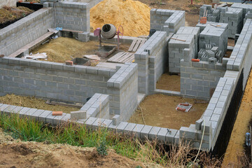 House under construction at a construction site. Mobile concrete mixer and concrete block building walls.