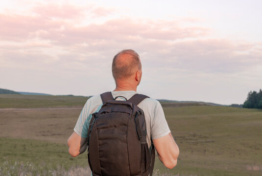 Mature man with backpack on back standing and enjoying sky view. Solo torist and hiker looking into the distance. Back view.