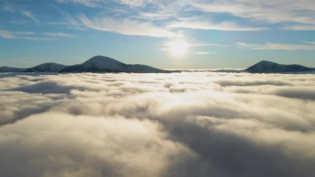 Aerial view of vibrant sunrise over white dense fog with distant dark peaks of Carpathian mountains on horizon.