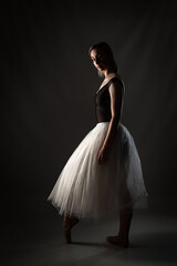 ballerina with a white dress and black top posing on gray background.