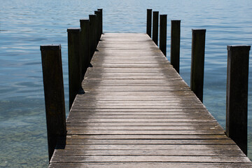 View down a small wooden jetty projecting into Lake Starnberg in Starnberg in Bavaria, Germany, on a sunny summer day