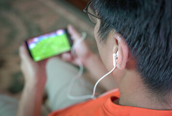 Man watching football and sports stream on mobile phone. Selected focus on ear phones.