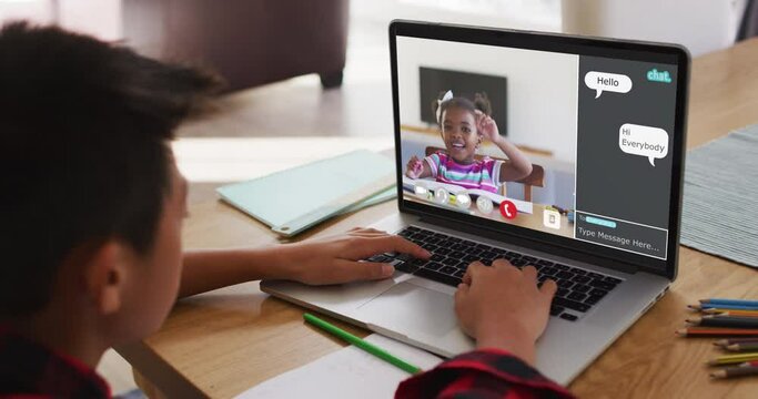 Schoolboy using laptop for online lesson at home, with girl raising hand and webchat on screen