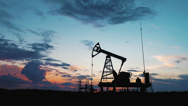 Silhouette working oil pump in deserted district at sunset. Oil drill rig and pump jack. Oil drilling derricks at desert oilfield for fossil fuels output and crude oil production from the ground.