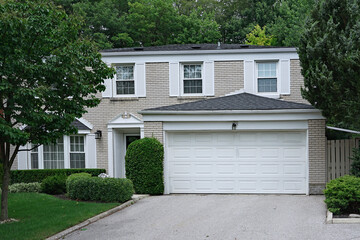 Suburban two story house with double garage and white bricks, surrounded by trees