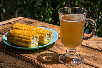 Beer and boiled corn on the cob. On wooden background, in fresh air. Topic: drinks and snacks