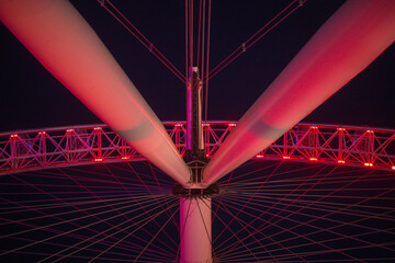 Low angle of rotating Ferris wheel details with red lights at night