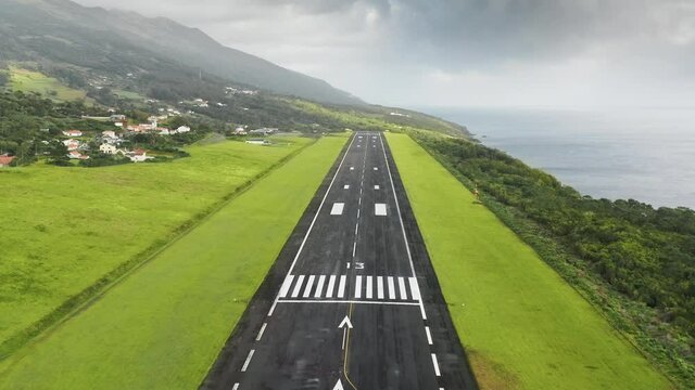 Aerial view of runaway of small airport at Sao Jorge island, Azores, Portugal, Europe. Overhead shot of green area of volcanic island with village houses surrounded mountains in summer time,4k footage