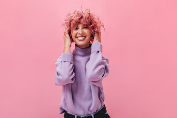 Pretty young woman in purple sweater smiles widely on isolated. Pink-haired girl looks into camera and laughs .