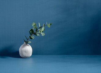 Minimalist still life scene. Ceramic ball-shaped vase and plant. Blue wall, sunlight and long...