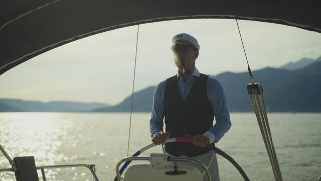 Sailor captain standing at steering wheel and navigation boat on calm sea, smoking pipe. Summer vacation at sea, sailing and travelling concept.