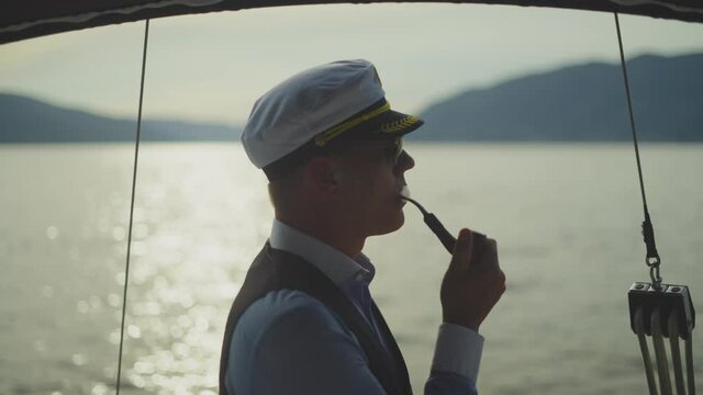 Side view headshot footage of mid adult sailor smoking pipe. Man sailing on boat. Summer vacation at sea, sailing and travelling concept.