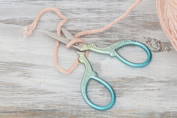 colorful embroidery scissors and pink yarn on white wood table 