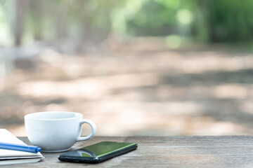 Holiday work concept of hot coffee mug with white paper book pen and mobile phone on wood table and Nature view in Rural village