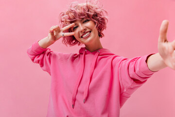 Close-up portrait of pink-haired woman in fuchsia color hoodie taking selfie on isolated...