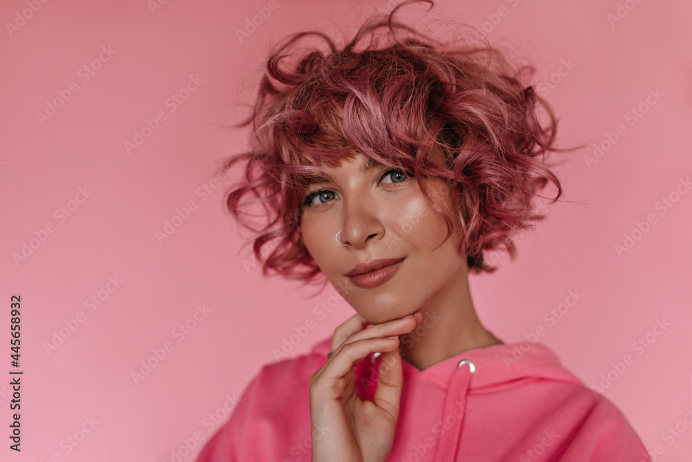 Wall mural Grey-eyed curly woman in pink hoodie smiles sincerely on isolated background. Happy young girl in bright outfit poses on pink backdrop. - Wall murals