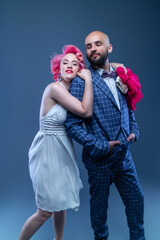 girl with short hairstyle and pink hair in a white dress and a bearded man in a blue suit on a blue studio background