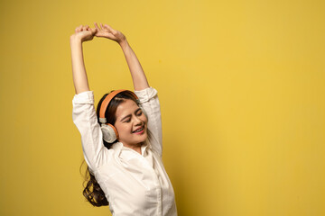 Young beautiful women listen to music via wireless headphone with yellow background, lifestyles concept