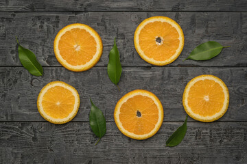 Pieces of fresh orange and leaves on a black wooden table. Flat lay.