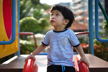 Happy little Asian boy having fun on the slide at an outdoor playground.