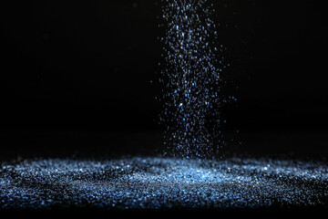 Shiny blue glitter falling down on black background. Bokeh effect