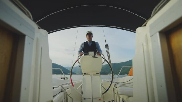 Sailor captain standing in cockpit and navigating boat. View from cabin entrance. Summer vacation at sea, sailing and travelling concept.