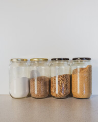 Vertical close up of glass jars with dry food ingredients including flour, ground flax, lentils and sugar on kitchen benchtop  with vintage filter effect and selective focus