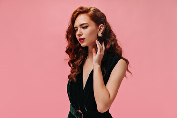Portrait of curly woman in velvet dress on pink background. Wonderful lady with ginger wavy hair in dark green outfit posing..