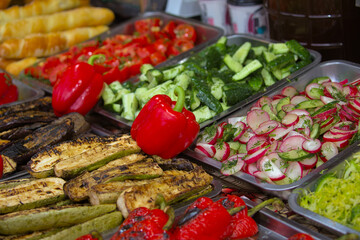 Healthy street food to go - red bell peppers, green cucumbers, red tomatoes, red and white sliced radishes, and more. Delicious food is offered at a street food fair, event, festival.