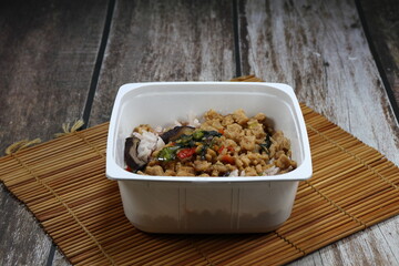 Classic lunch box menu in Asia. Traditional spicy fried mince pork with basil topping on cooked jasmine rice serving in the plastic box.