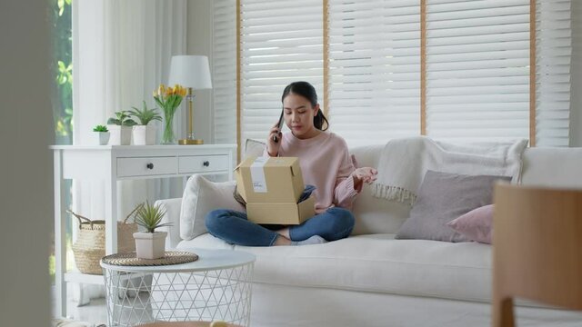 Upset mad asia people young girl consumer sit sofa at home open fake product order, damage post mail buy from online shopping retail store. Shock sad teen woman unbox from wrong bad shipping service.